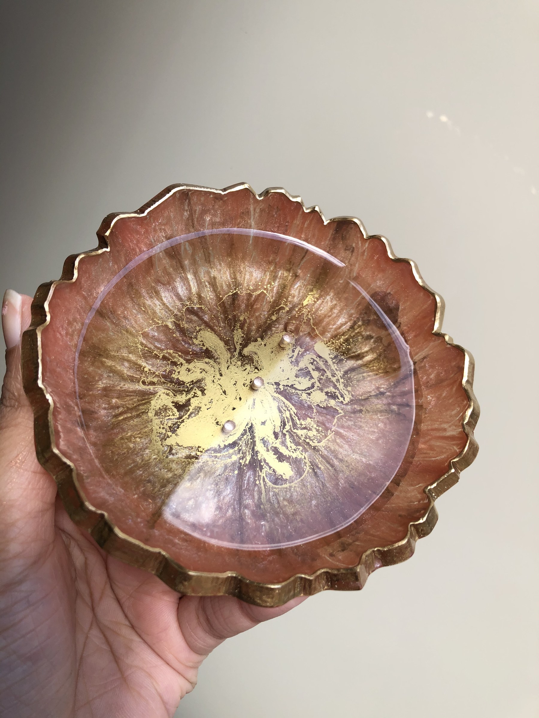 Close-up of a rose gold resin coaster with gold ink swirls