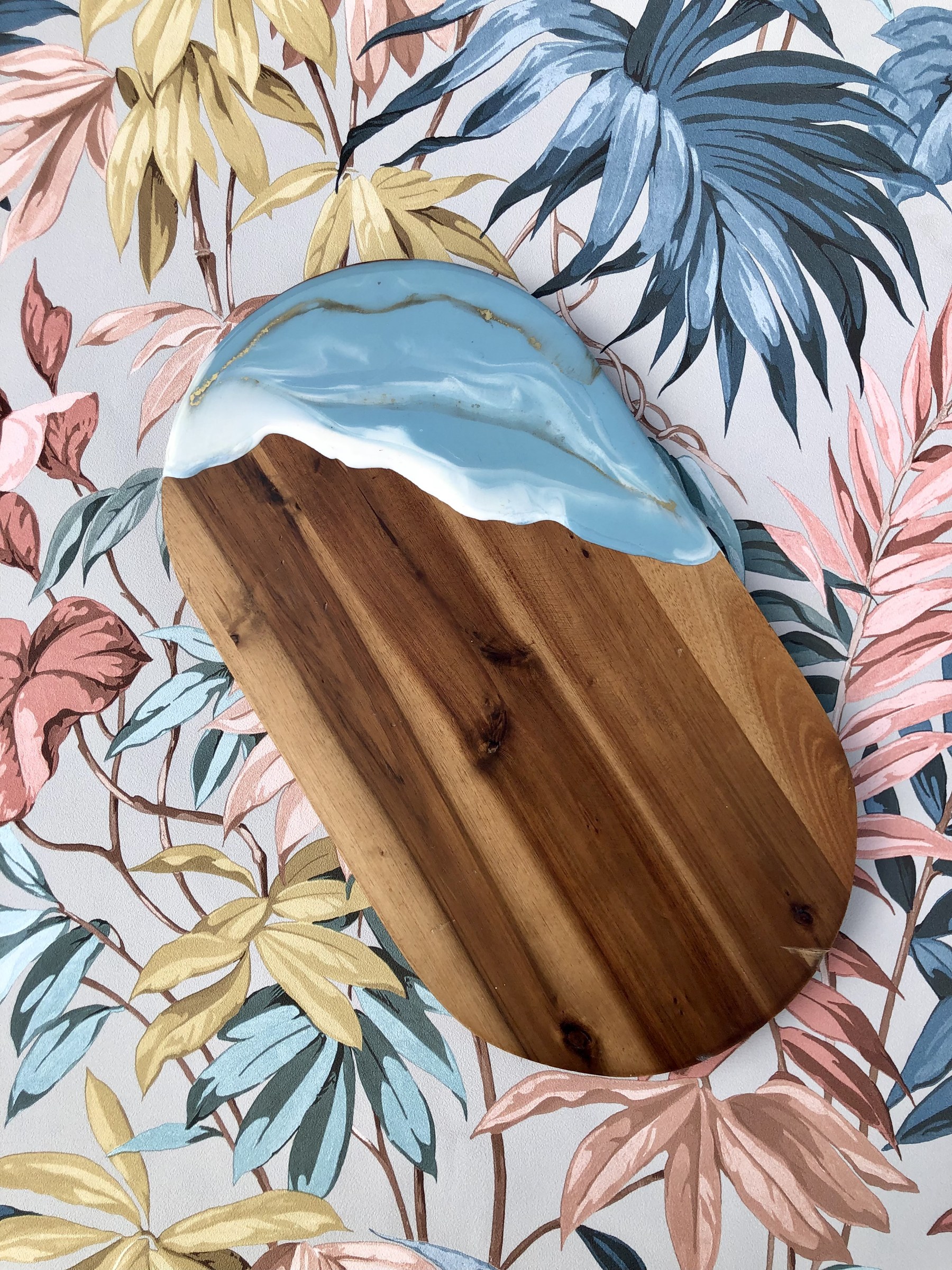 Acacia cheeseboard with sky blue resin pour on tropical floral backdrop